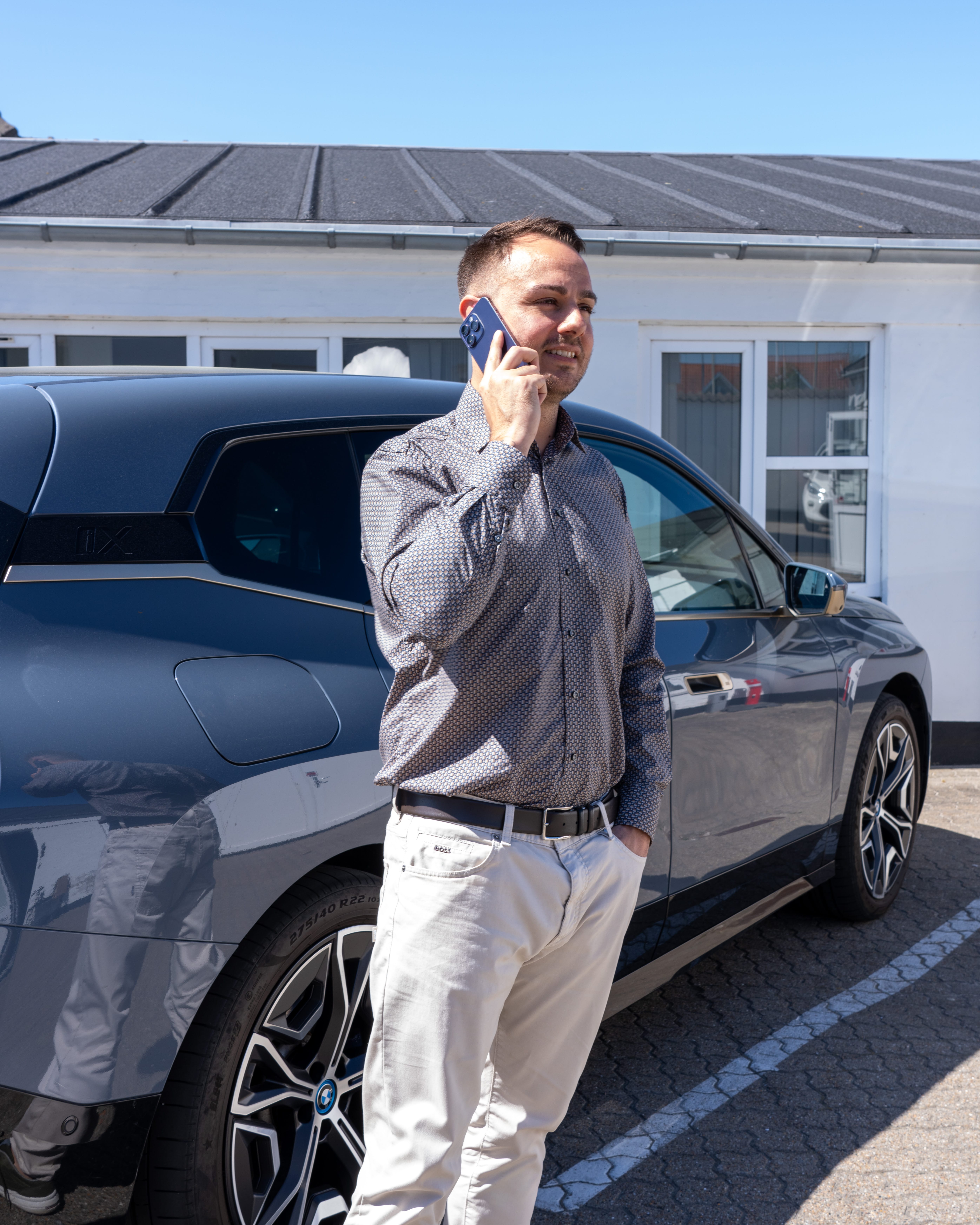 Mand taler i telefon ved bil foran bygning