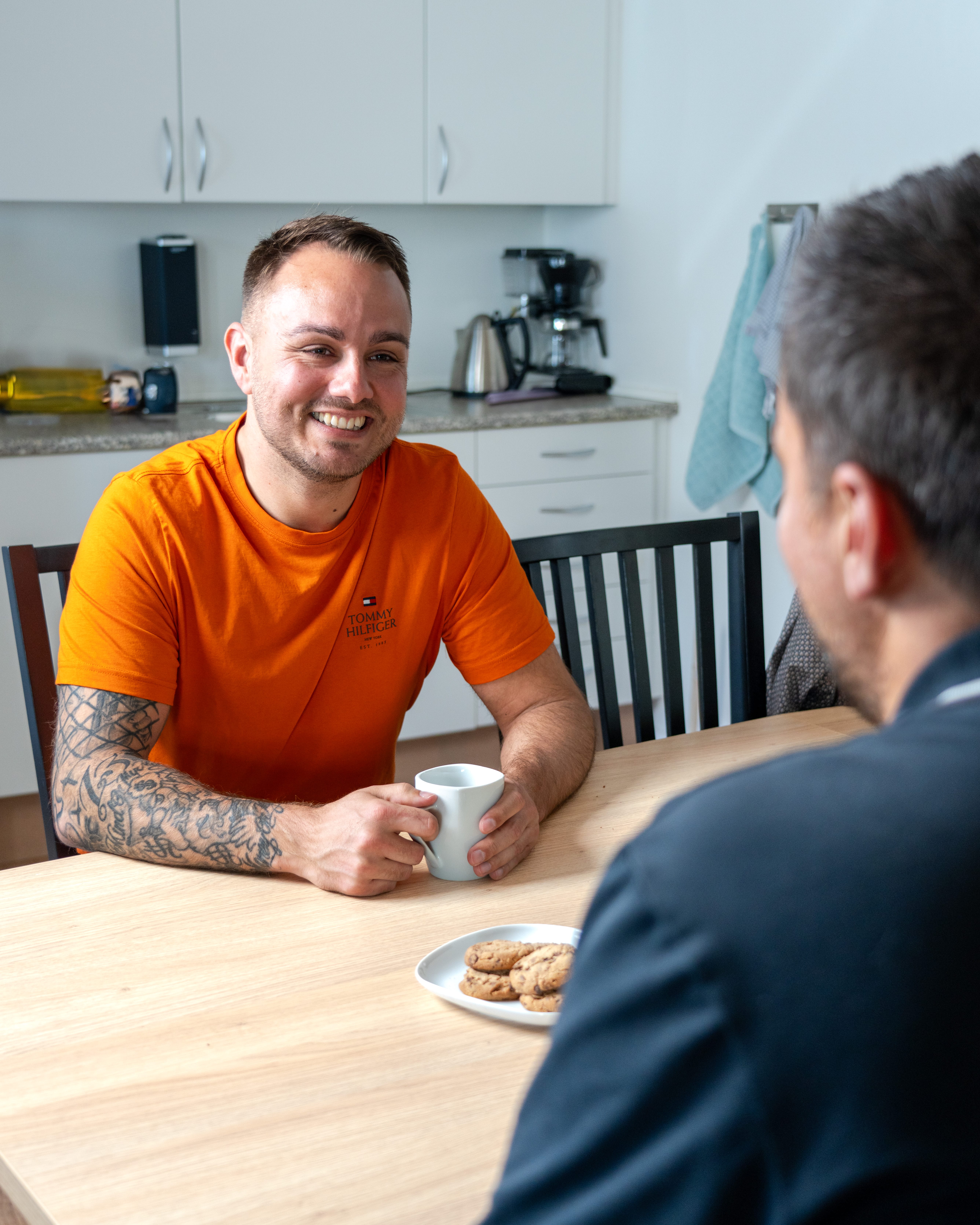 To mænd drikker kaffe og taler ved køkkenbordet